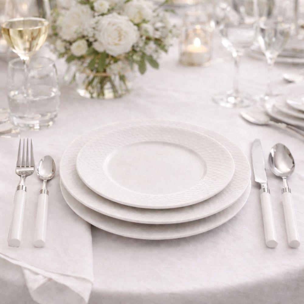 Set posate in uso su tavola apparecchiata con piatti bianchi, bicchieri e vaso di fiori su tovaglia bianca